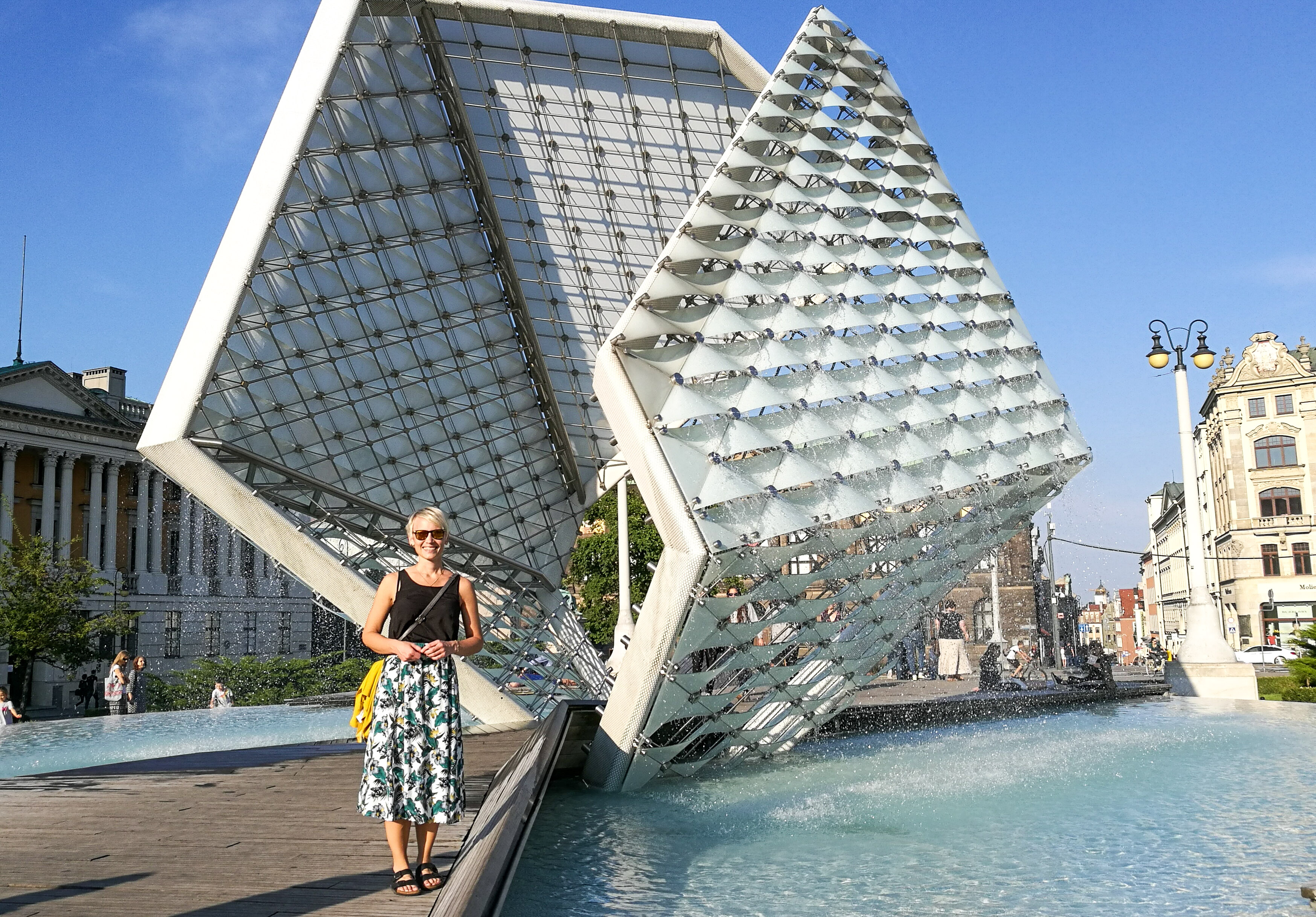 a woman in skirt standing in front of a modern fontain in Poznan