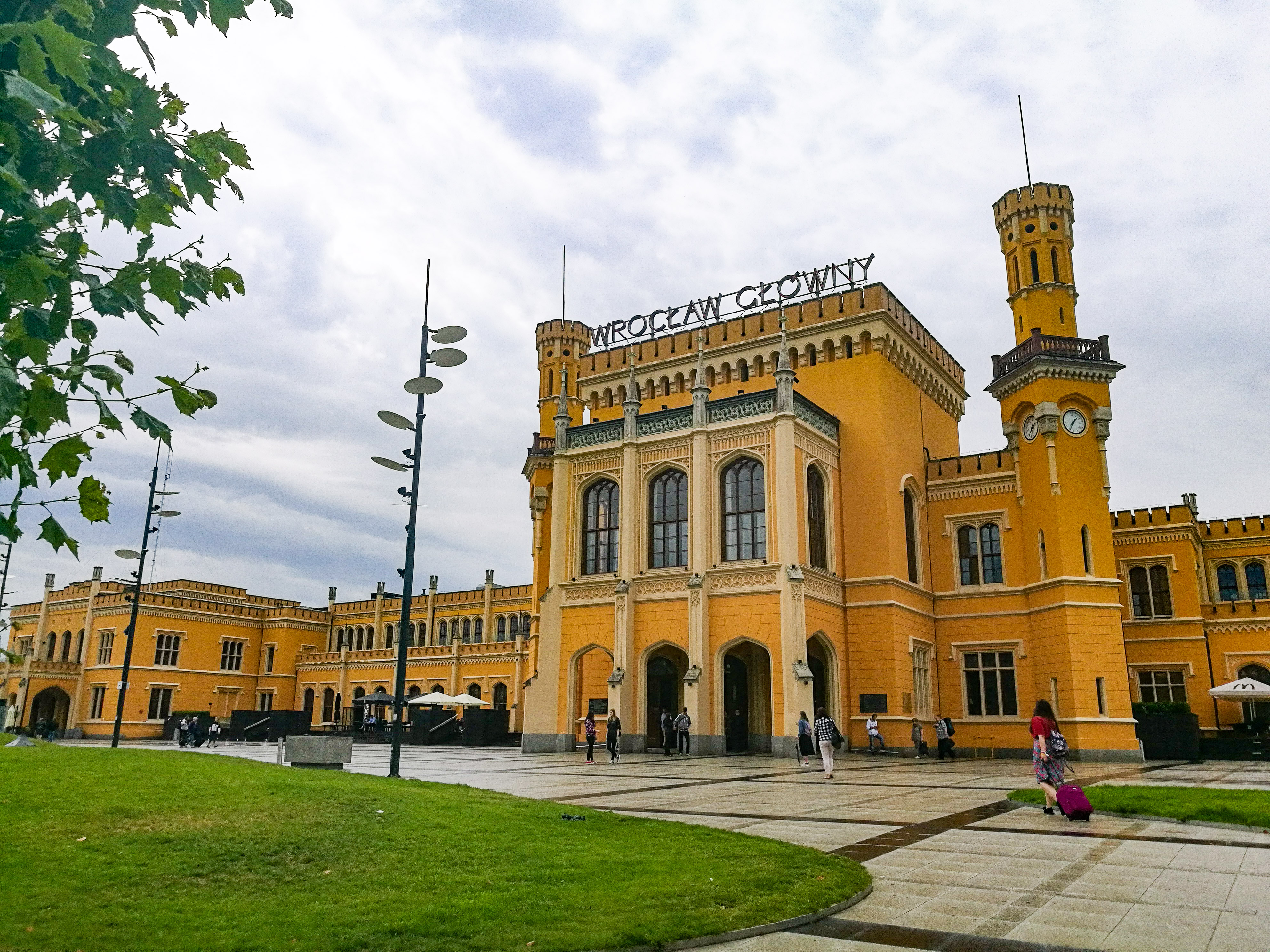 The yellow station building in Wroclaw with two spires and people walking outside.
