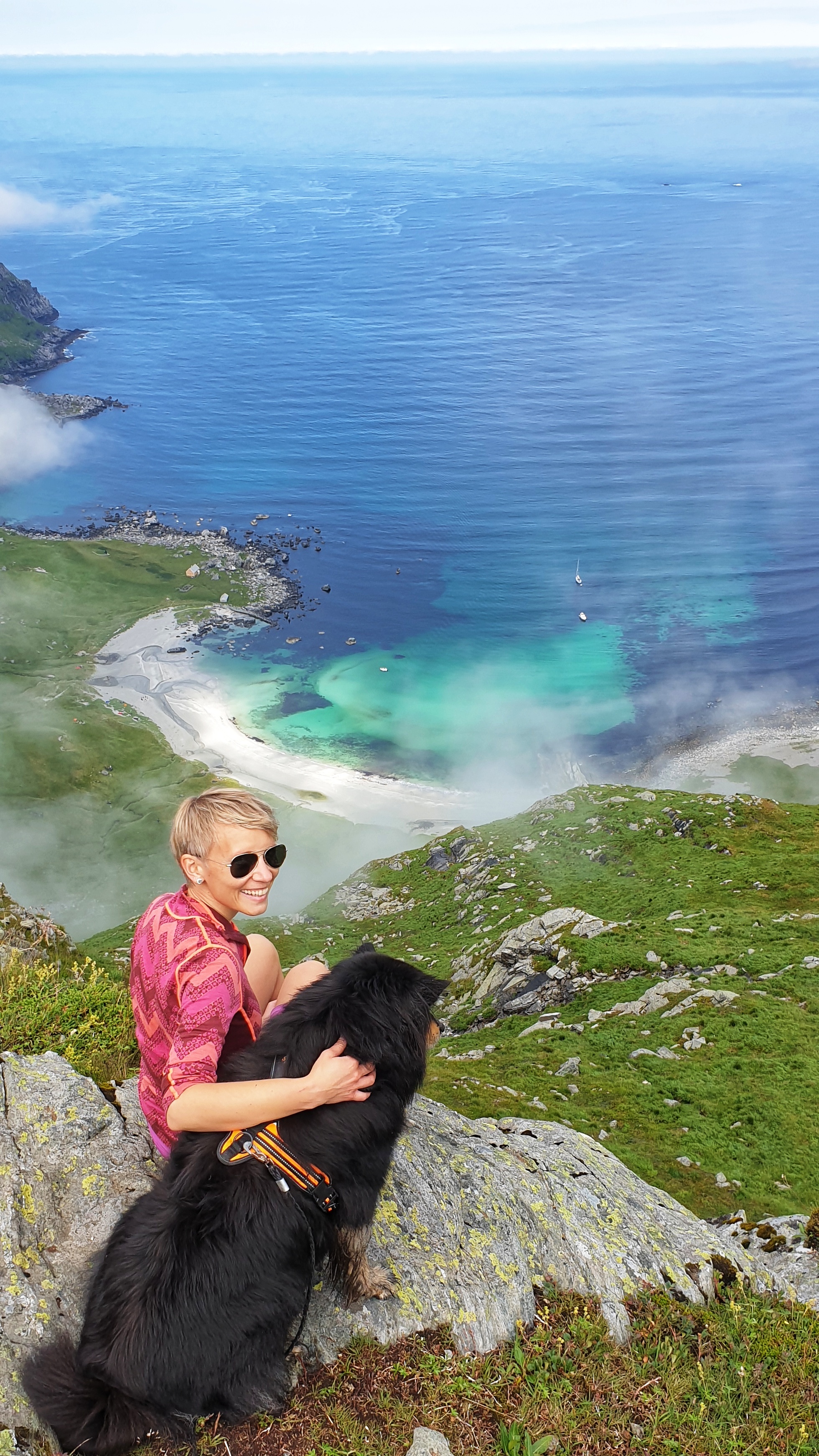 A smiling woman and a dog sitting above Vetvika beach in Western Norway