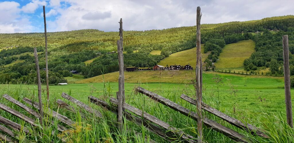 An old farm in Heidal seen behind a fence surrounded by green fields