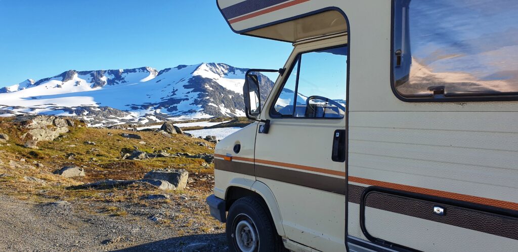 An old camper parked in the Norwegian mountains. Snow-covered peaks in the distance.