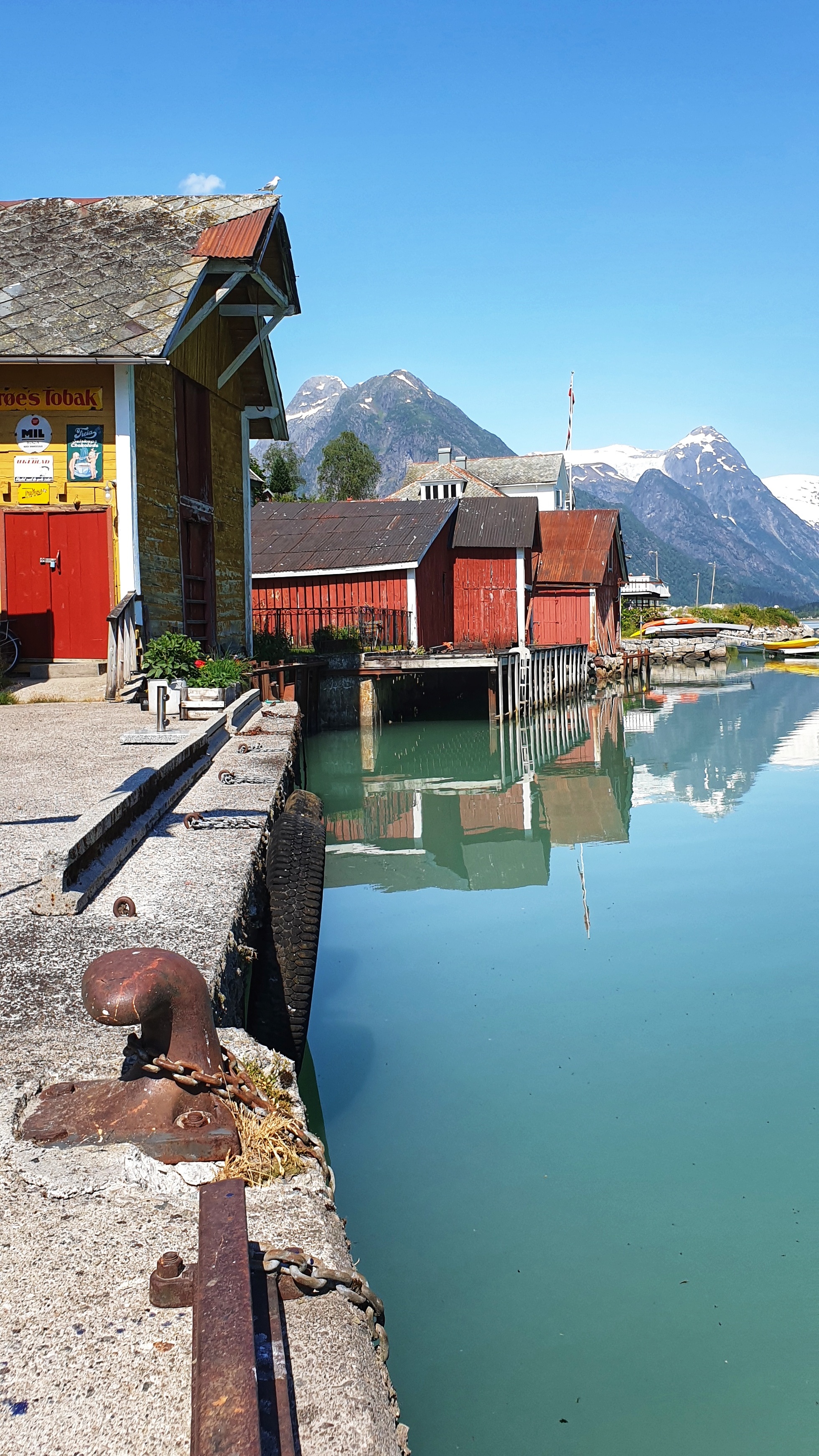 One yellow and three red boat houses by the FjÆrlandsfjord, with mountains and glacier behind.