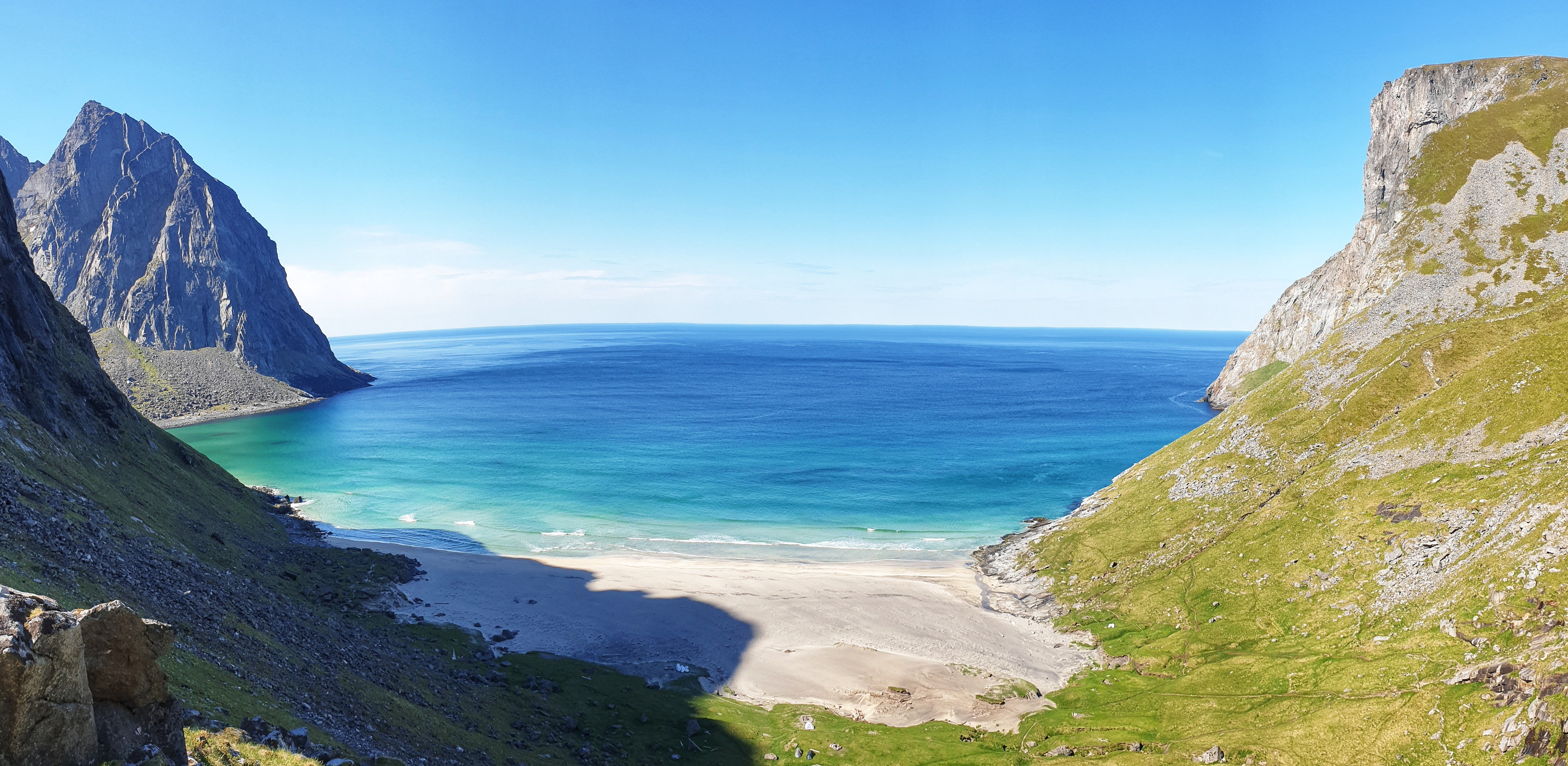A white sand beach between mountains, meeting clear blue sea at Kvalvika.