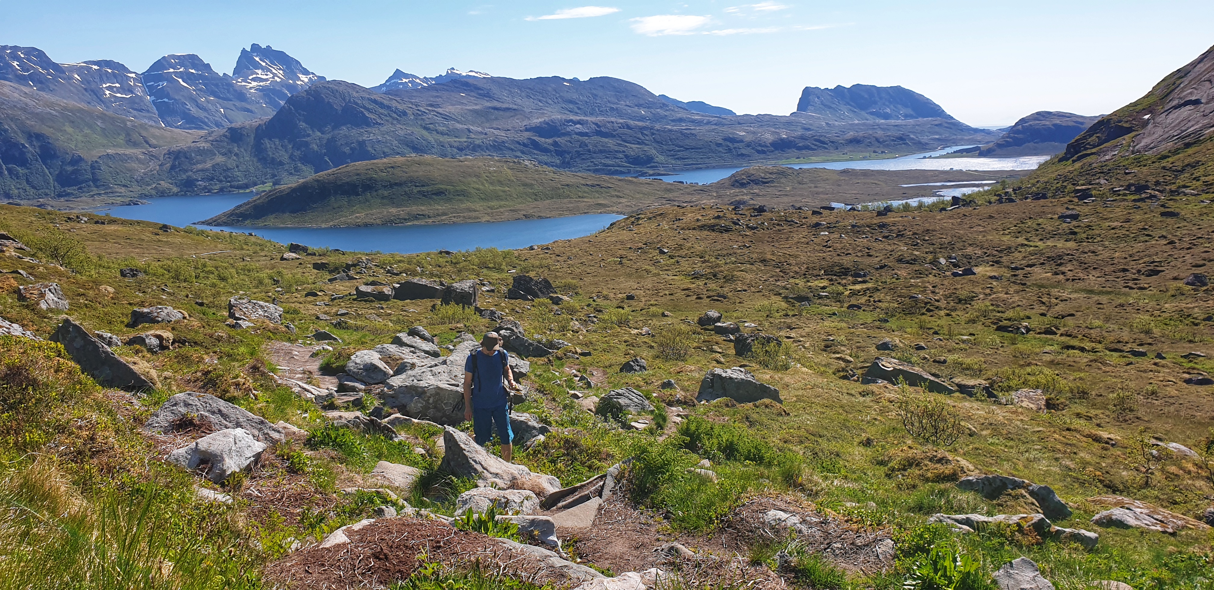 A man hiking on a gentle hill. Sea and rugged peaks behind him.