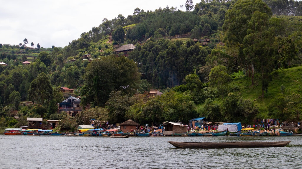 The colourful Friday Market at Lake Bunyonyi seen from the lake with steep green hill above.
