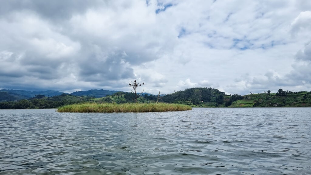 View of the small Punishment Island on Lake Bunyonyi. Rolling green hills in the back and cloudy sky.