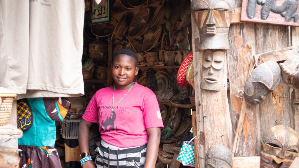 A girl in a pink t-shirt standing in a small souvenir shop in Bwindi in Uganda. Carved maskes and more in the background.