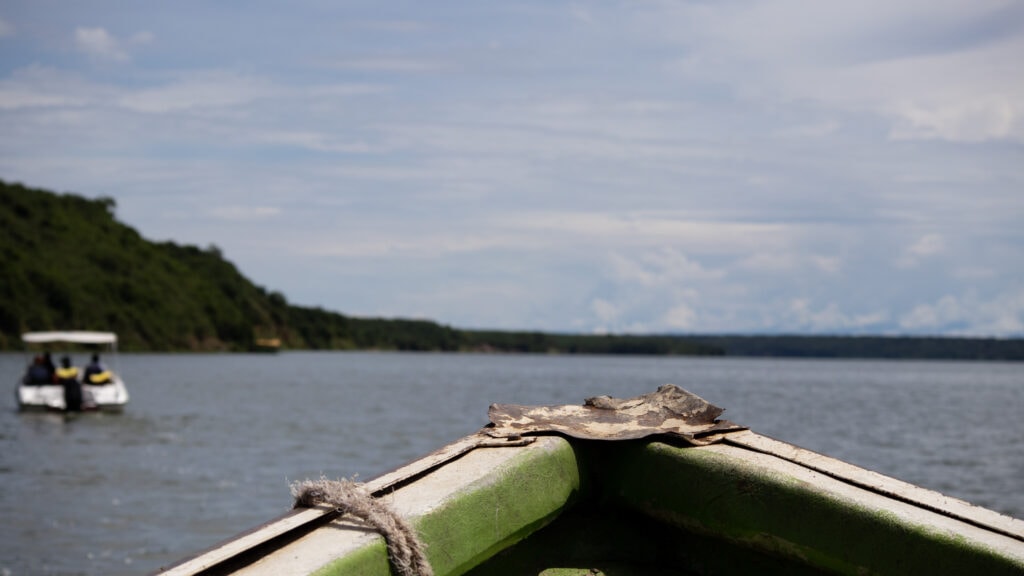 The front of a green boat on the Kazinga Channel, a small white motor boat in front.