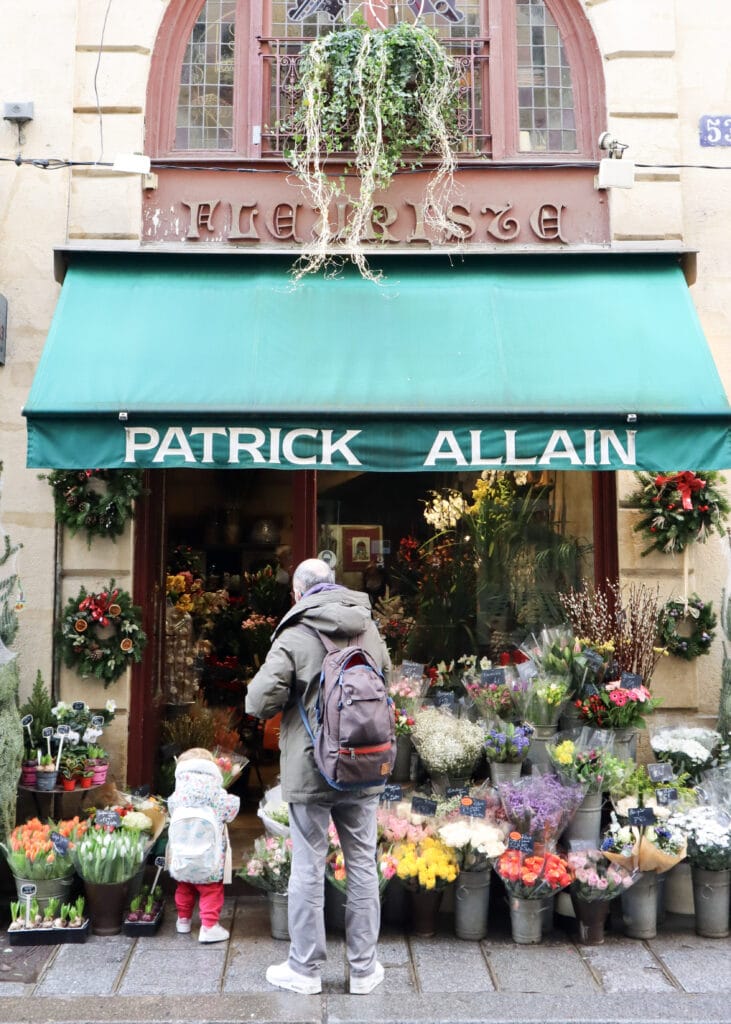 A man and a child outside a flower shop. The small child holding a bouquet.