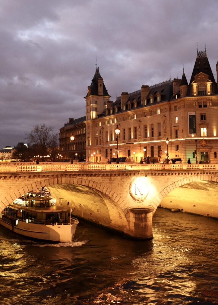 A boat sailing underneath a bridge on the Seine on a December evening in Paris.