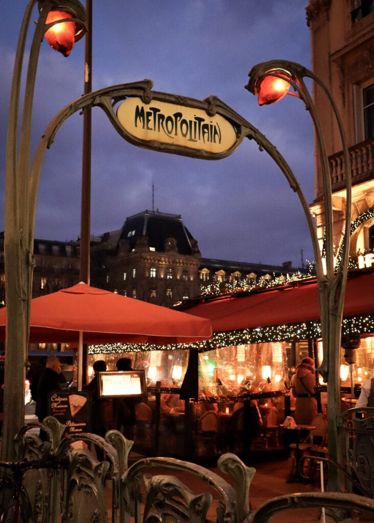 The art nouveau Saint-Michele metro station with Christmas illuminated restaurant behind.