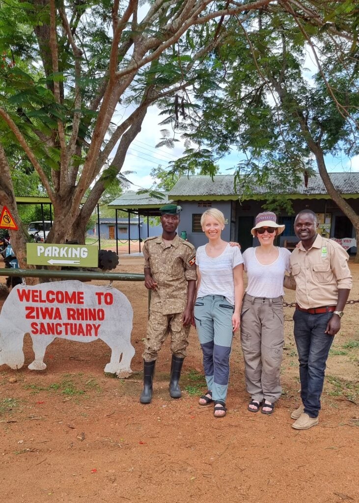 Two women standing between two men in guide outfits by a welcome sign at Siwa Rhino Sanctuary.