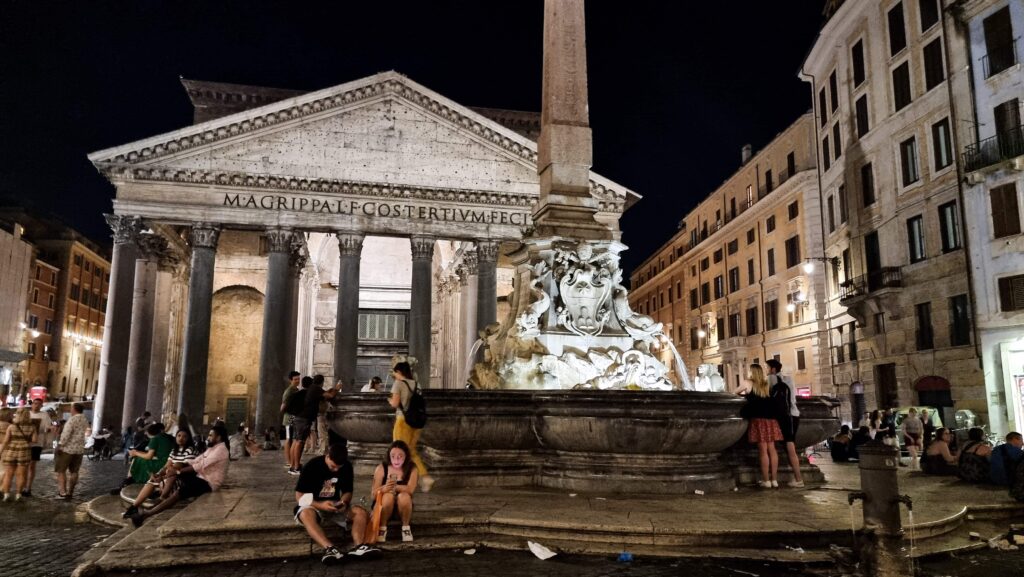 People sitting and standing on steps in front of Phanteon in Rome.