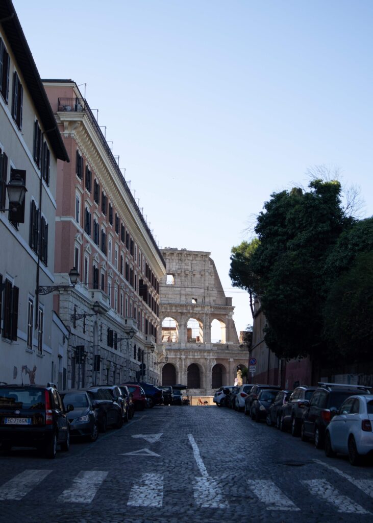 Colosseum seen at the end of a street lined with cars.