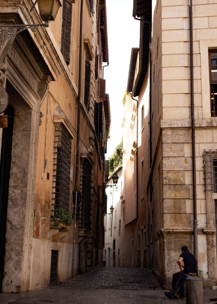 A man sitting near an alley in Rome, looking at his phone.