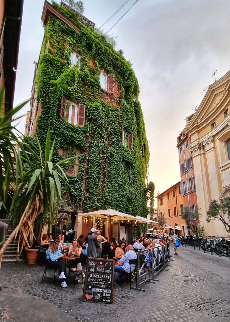 People sitting outside on a restaurant, the facade covered on climbing plants.