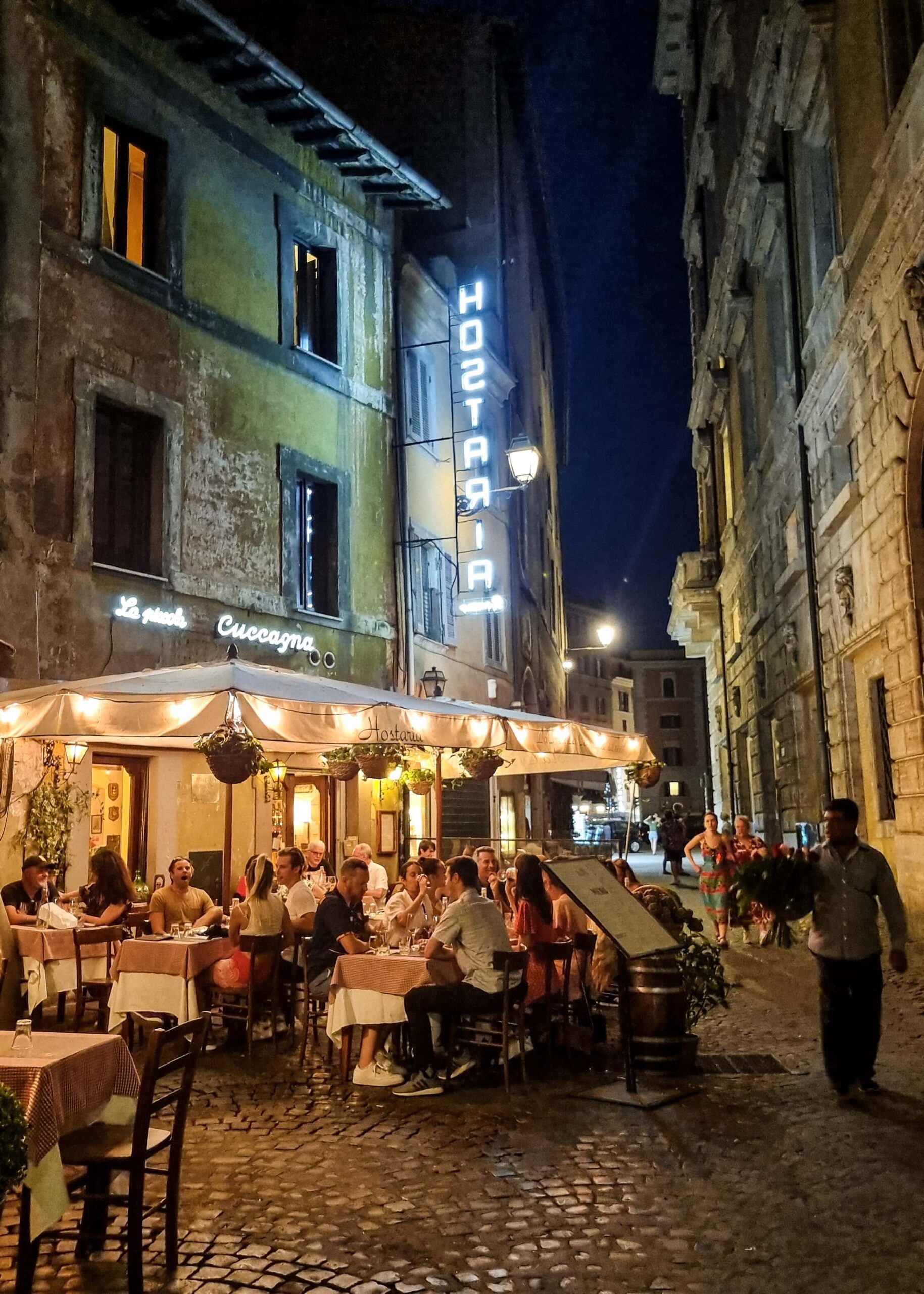 Street restaurant full of dining people, a man selling roses walking by.
