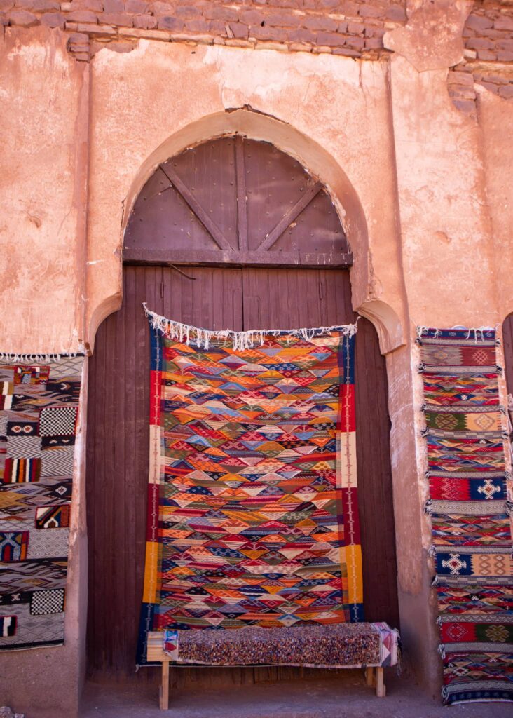 A large, colourful Moroccan rug hanging on a large wood door. Two smaller rugs hanging on each side.
