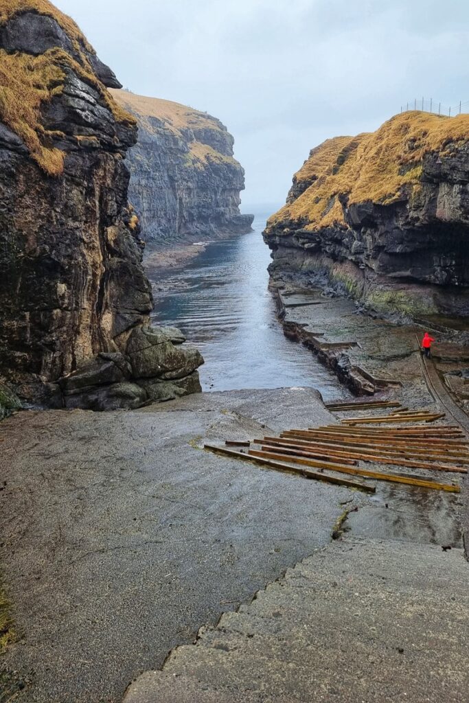 A person in red jacket walking down into Gjogv's bay on the Faroe Islands.