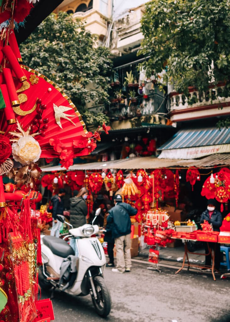 Bright red decorations for sale on two sides of the road. A parked, white motorbike in the middle.
