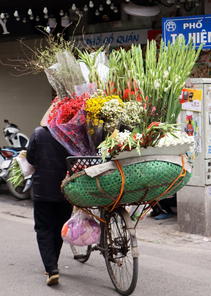 A woman walking a bike filled with fresh flowers in Hanoi.