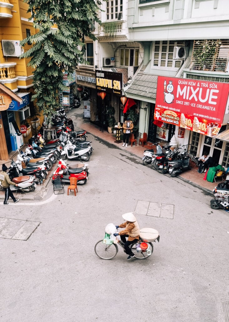 A person seen cycling through a street in Hanoi from above.