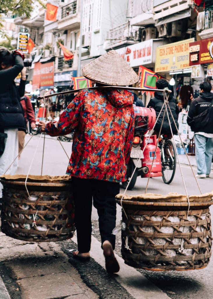 A woman carrying large baskets from a pole across her sholder.