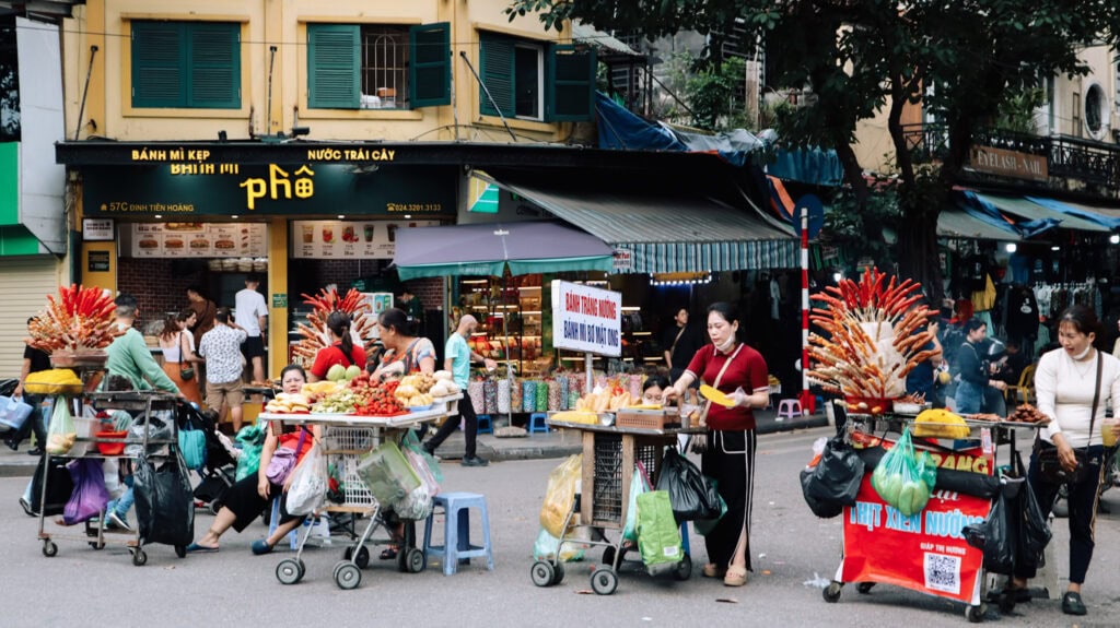 Street vendors standing on the evening walking street in Hanoi selling colourful food.