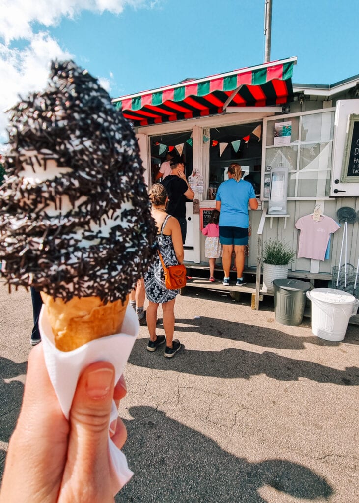 A hand holding an icecream in front of a small stall in Arild, Sweden.