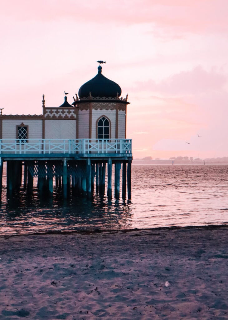 Varberg Kallbadhus bathing in pink light at sunset. Two birds flying over the sea.