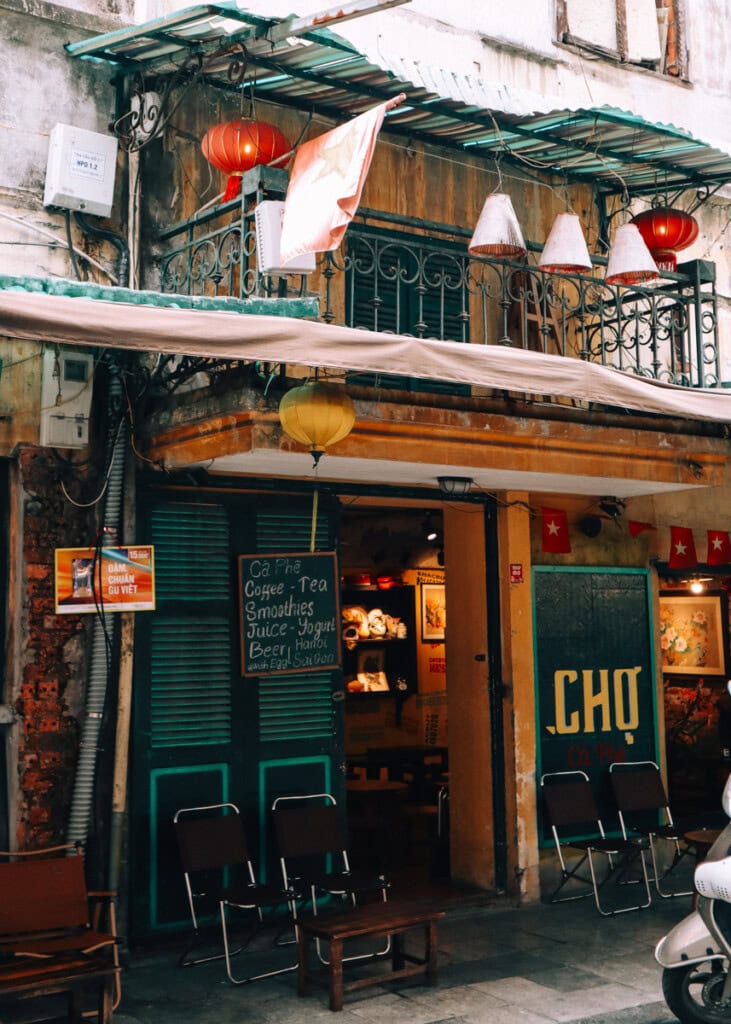 Entrance of Cua Hang Ca Phe, decorated with lanterns, Vietnamese flags and handwritten signs. Chairs outside.