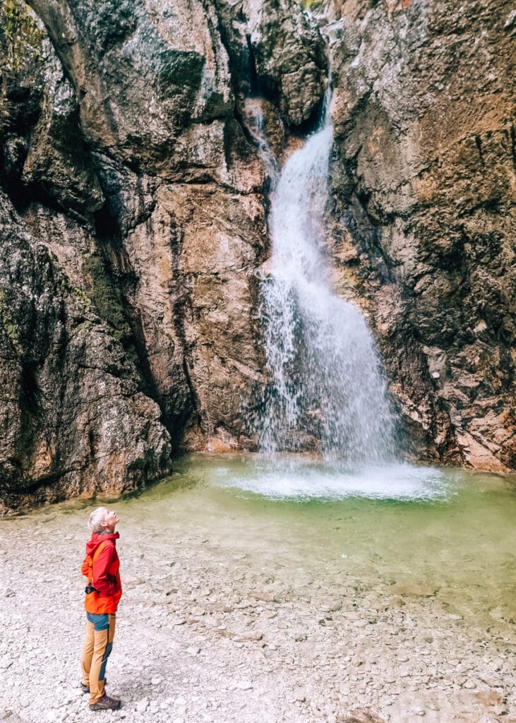 A woman wearing colourful hiking clothes looking up at Slap Katedrala in the Soca Valley.