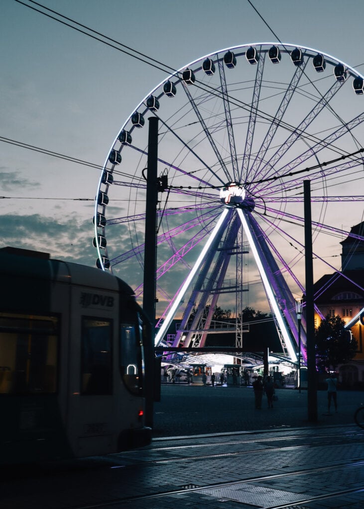 A tram in front of a ferris wheel in Dresden at night.