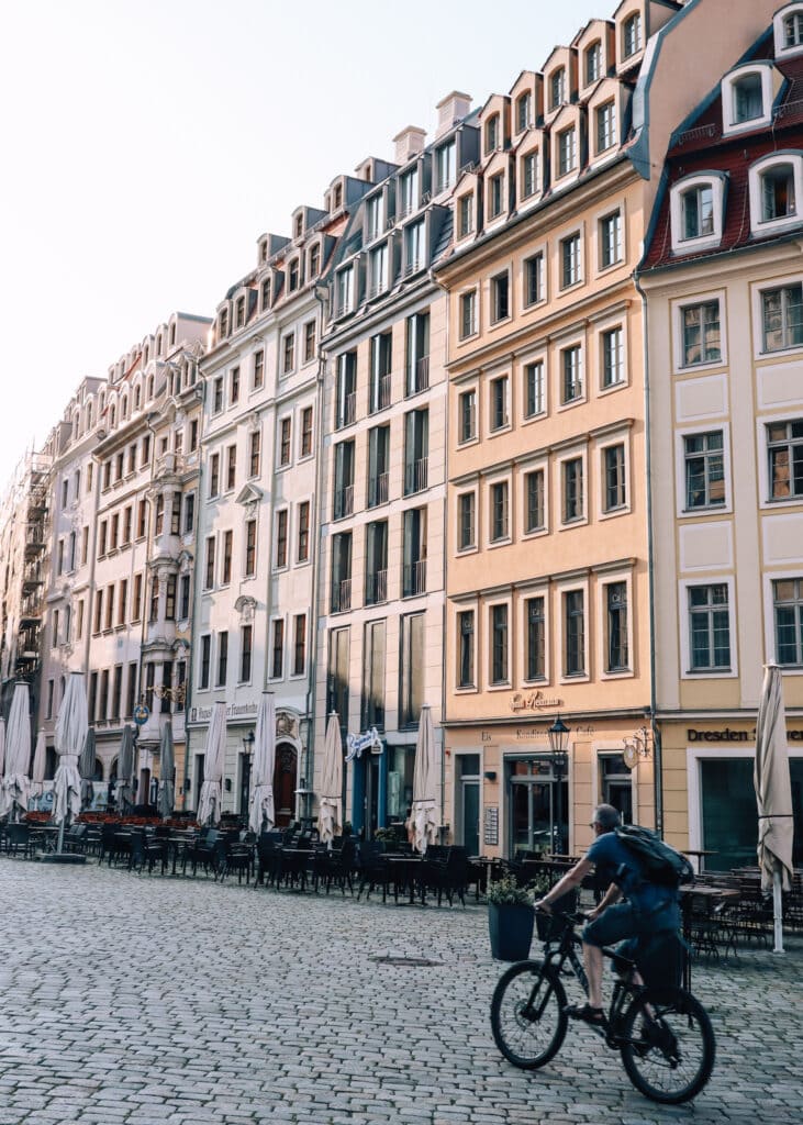 A man cycling past pretty buildings and empty restaurants on an morning in Dresden.
