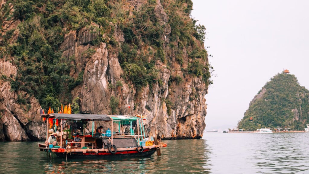 A colourful, local wooden boat with roof next to a limestone carst in Halong Bay.