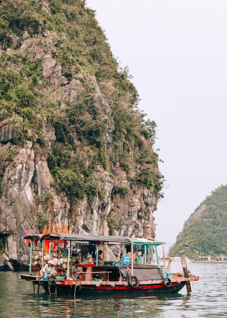 A local wooden fishing boat with roof in front of a typical karst in Halong Bay.