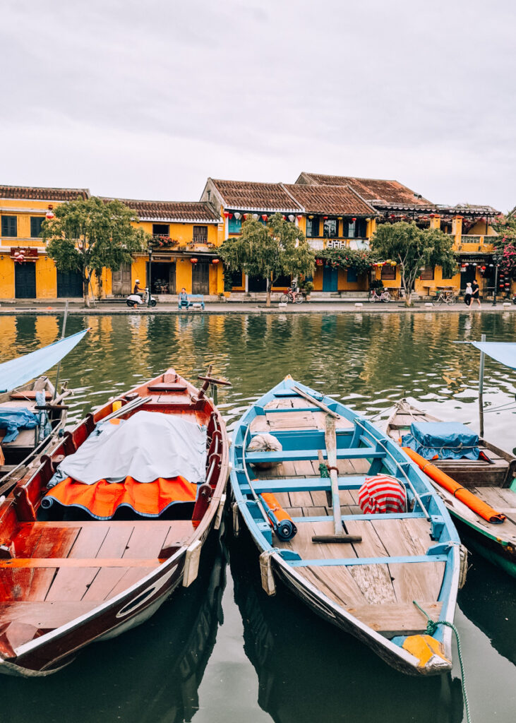Wooden boats on the river in Hoi An, a row of yellow houses behind.