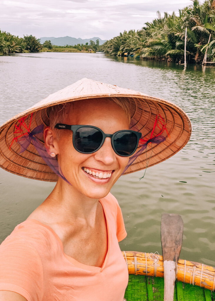 Selfie of Anne (writer) smiling under a conical hat on the river in the Coconut forest in Hoi An.