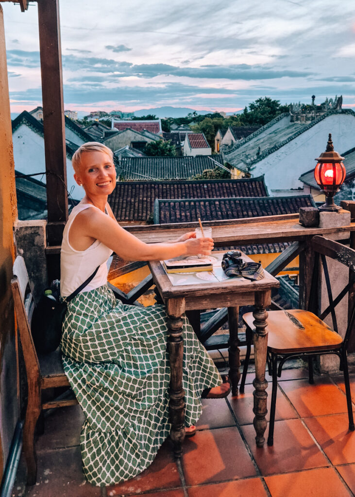 A woman strecthing for a drink at a rooftop restaurant in Hoi An at sunset.