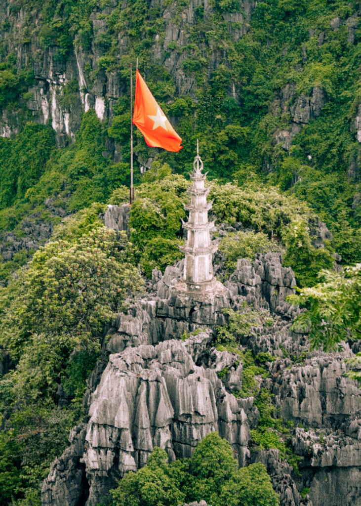 An ornamented tower next to a large Vietnamese flag on a mountain near Hang Mua in Ninh Binh.