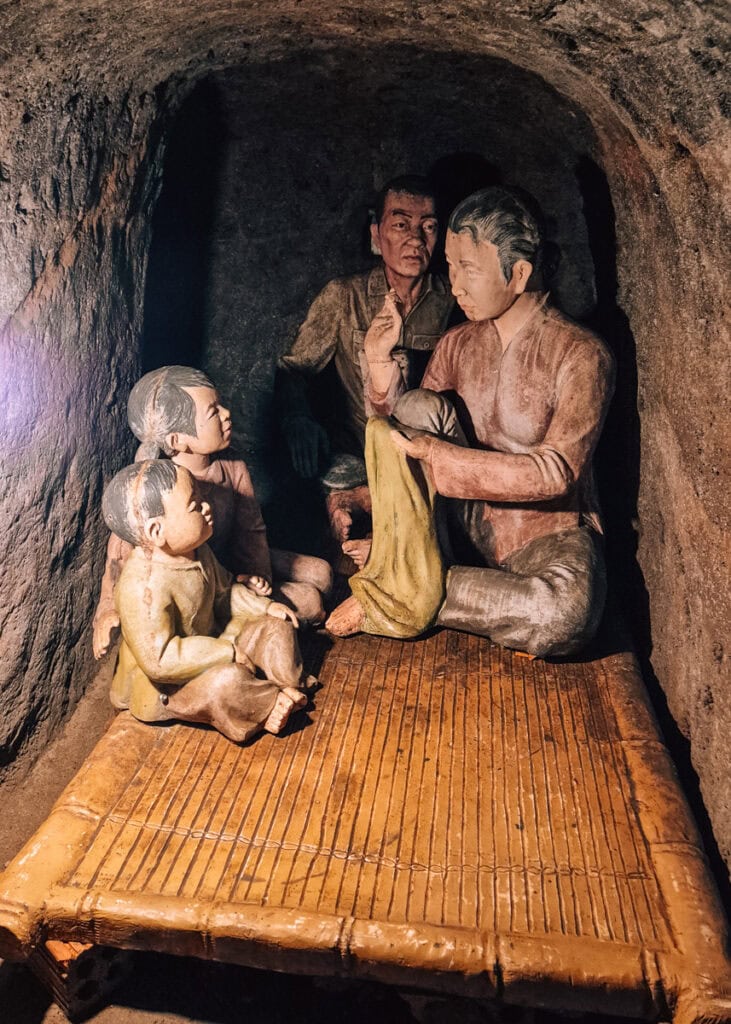 Picture of a family room in a Vinh Moc tunnel. Real life sized sculptures of a family sitting on a bed that takes up all space.