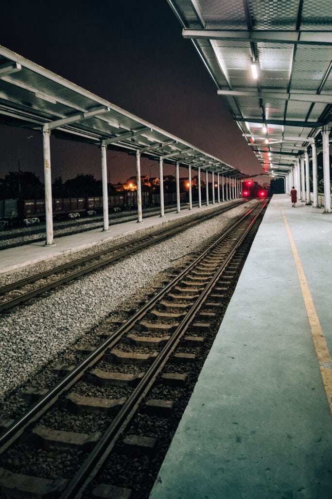 An empty platform at Ninh Binh Railway Station at night. One woman in a red dress walking away.