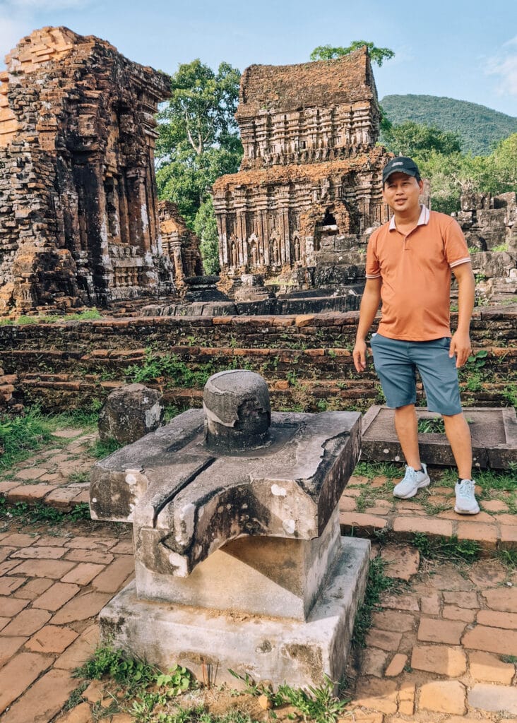 A guide at My Son standing by a an alter symbolising both a vulva and a fallos. Temples seen behind.