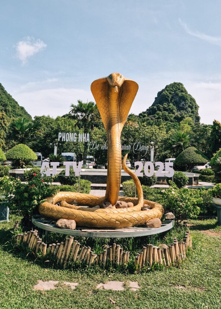 A golden statue of a cobra snake in front of a sign of Phong Nha in the town centre.