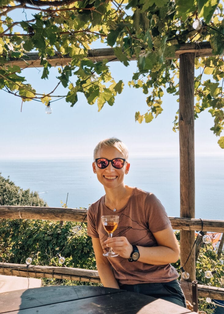 Me (Anne) holding a glass of local wine at a bar along the trails. View to the sea behind me.