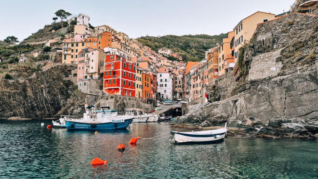 The colourful and steep town of Riomaggiore with fishing boats docked on the clear blue water.