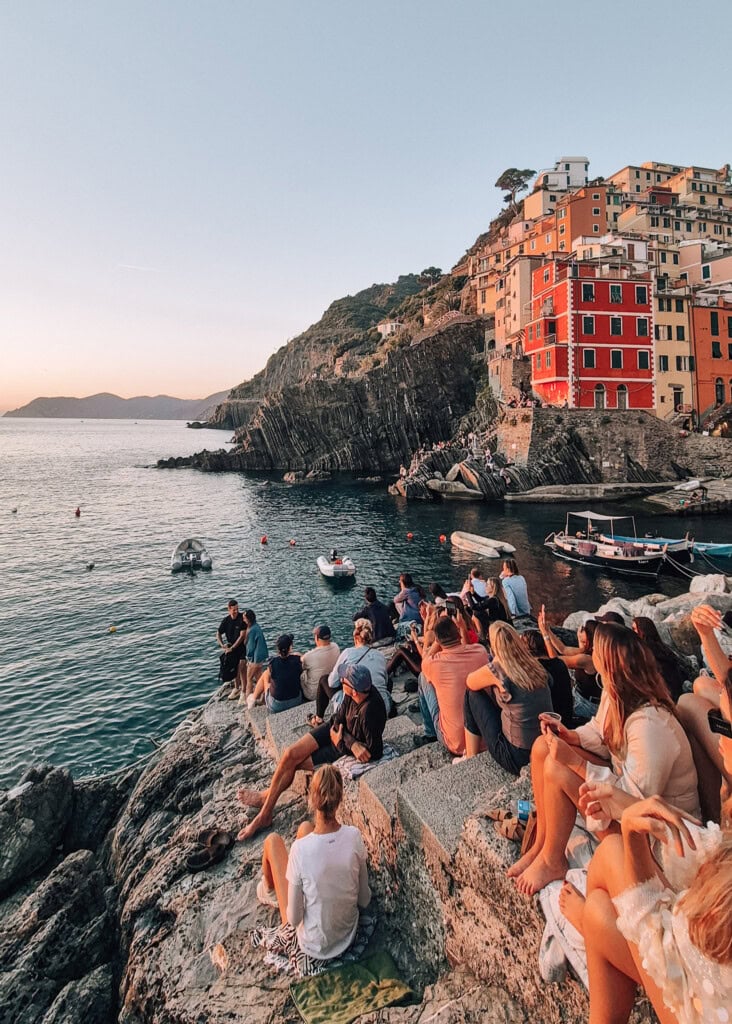 People sitting on the rocks watching the sunset in Riomaggiore.