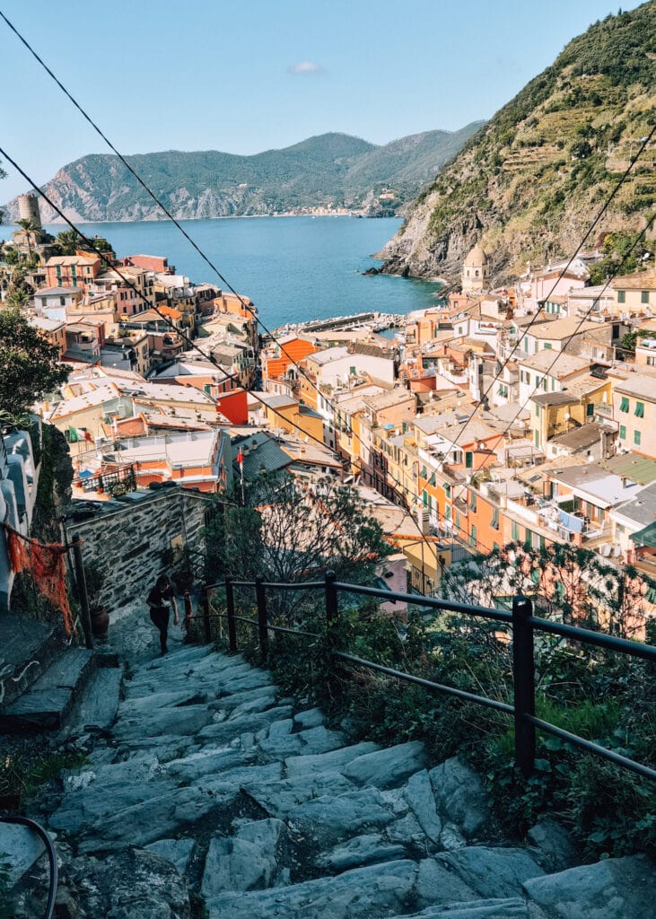 Stairs going up from Vernazza which is seen below. A woman walking up.
