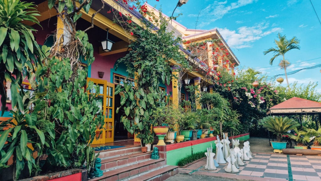The colourful facade of Phong Nha Farmstay with lots of green plants in front.
