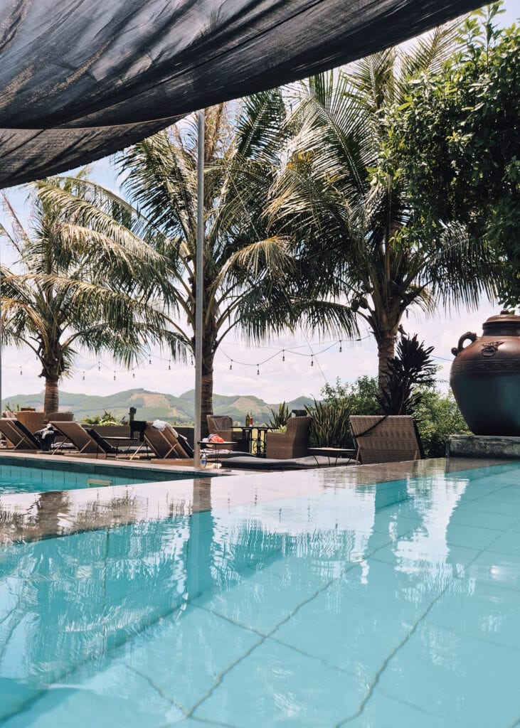 The pool at Phong Nha Farmstay. Sunbeds, sitting groups and palm trees behind.